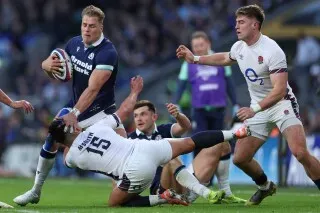 لاعبو الرجبي الاسكتلنديون في مباراة ضد إنجلترا، حيث يتجاوز أحدهم لاعباً منافساً أثناء الهجوم، مما يعكس الحماس والتنافس في بطولة الأمم الستة.