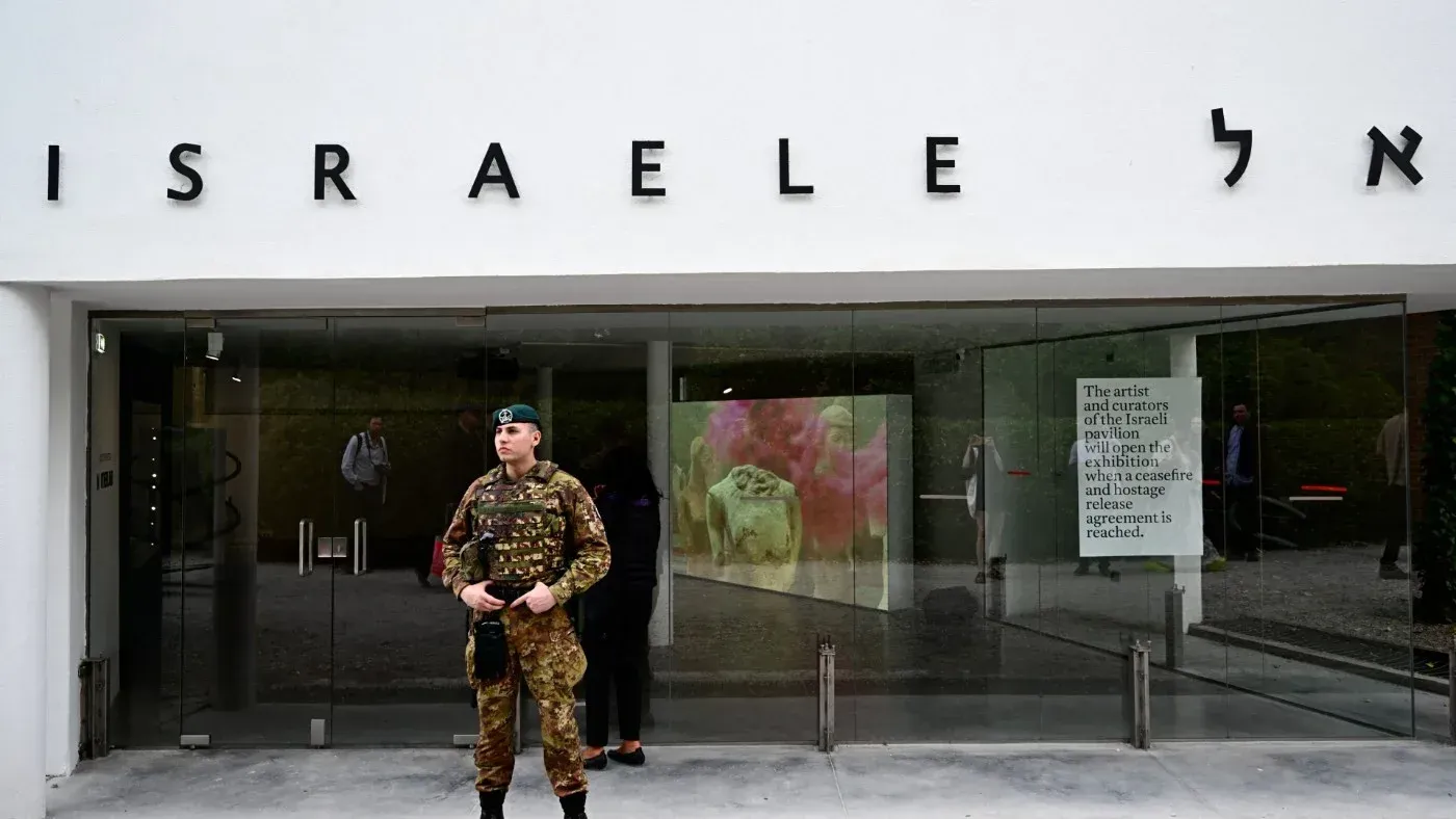 مدخل جناح إسرائيل في بينالي البندقية، حيث يظهر جندي أمامه، مع لافتة تشير إلى شروط افتتاح المعرض.