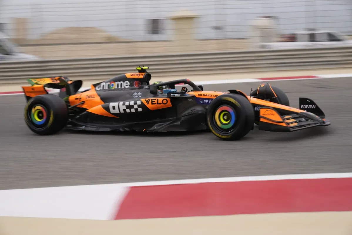 سيارة سباق مكلارين F1 تتسابق في حلبة البحرين، مع تفاصيل ملونة للعجلات وتصميم ديناميكي، تعكس المنافسة بين ماكس فيرستابن ولاندو نوريس.