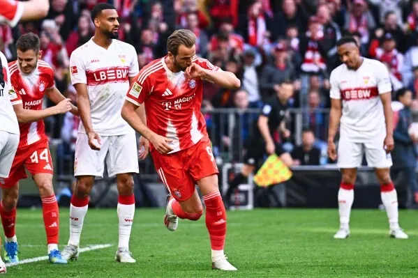 هاري كين يحتفل بتسجيل هدف مع بايرن ميونيخ في مباراة بالدوري الألماني، محاطًا بزملائه في الفريق، مع التركيز على أدائه المتميز هذا الموسم.