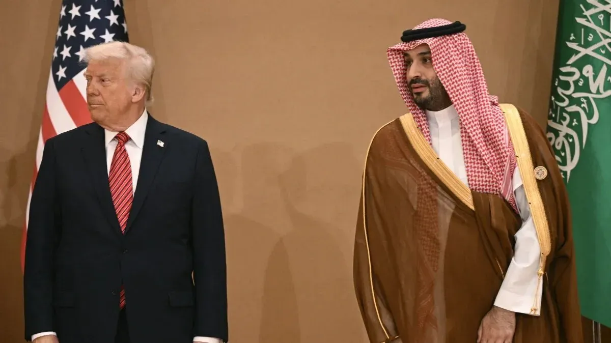 لقاء بين الرئيس الأمريكي السابق دونالد ترامب وولي العهد السعودي محمد بن سلمان، مع العلم السعودي والأمريكي في الخلفية، يعكس العلاقات السياسية.