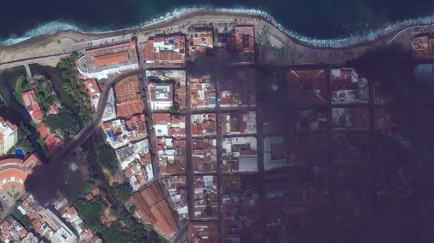 دخان كثيف يغطي مدينة بويرتو فالارتا المكسيكية بعد أعمال عنف، مع تضرر المباني والسيارات، مما يعكس حالة الفوضى في المنطقة.