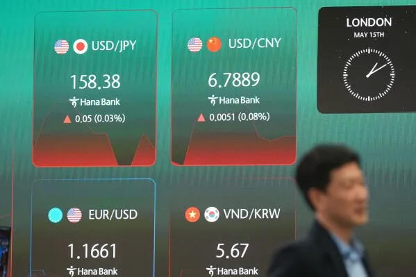 شاشة تعرض أسعار صرف العملات الأجنبية، بما في ذلك الدولار الأمريكي مقابل الين الياباني واليوان الصيني، مع شخص يمشي في الخلفية.