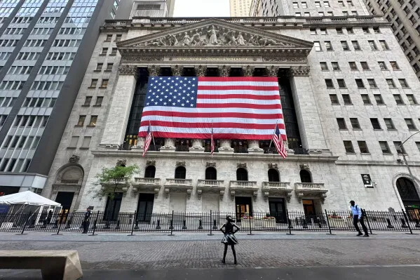 واجهة بورصة نيويورك مزينة بعلم الولايات المتحدة الكبير، مع مشهد للمتسوقين في الشارع، مما يعكس النشاط الاقتصادي في ظل تقلبات السوق.