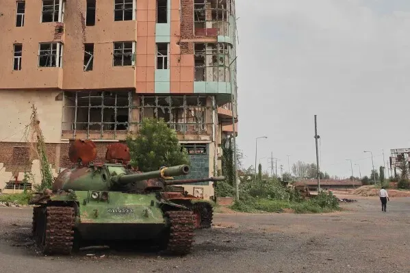 دبابة مدمرة أمام مبنى متضرر في الخرطوم، تعكس آثار النزاع المستمر في السودان وتدمير البنية التحتية.