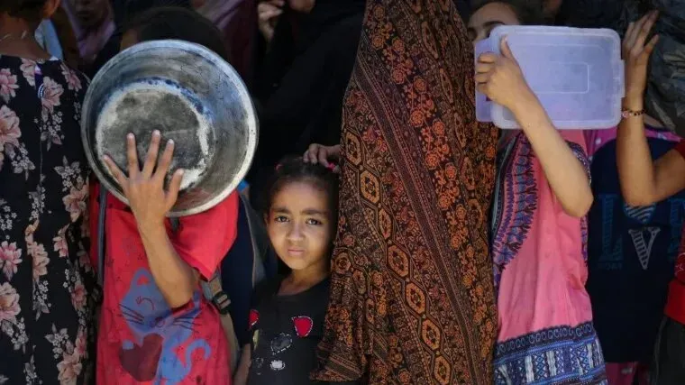 طفلة تنظر بقلق بينما تقف بين النساء في طابور للحصول على الطعام، تعكس معاناة سكان غزة في ظل أزمة إنسانية خانقة.