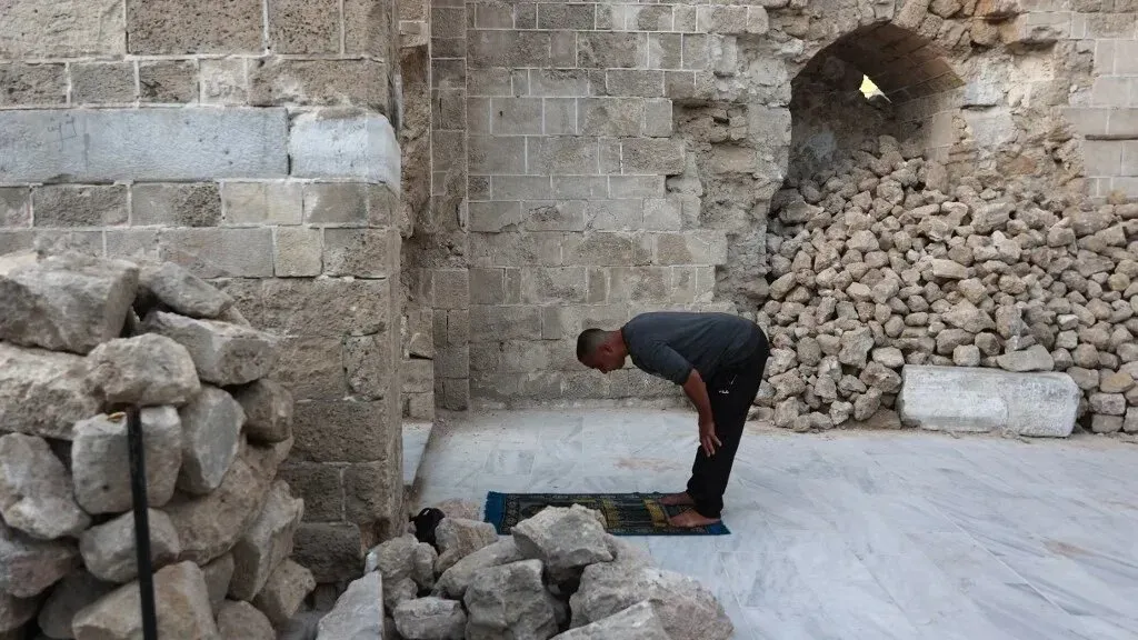 رجل يؤدي الصلاة في مكان دمرته الحرب، محاطًا بحطام الحجارة، معبرًا عن الإيمان والصمود في وجه المعاناة.