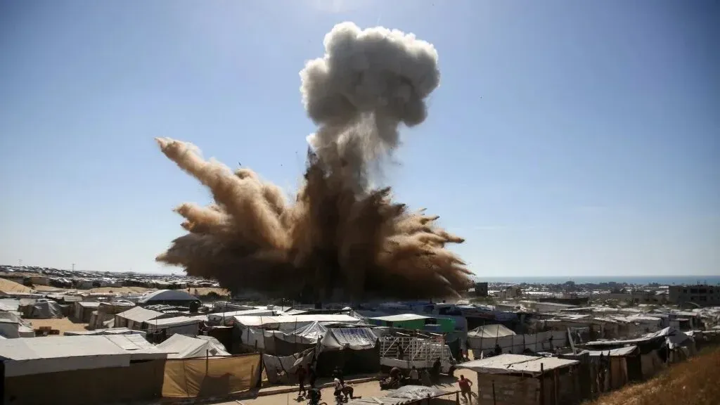 انفجار كبير يثير سحابة من الغبار فوق مخيمات في غزة، يعكس تصاعد العنف في الصراع الإسرائيلي الفلسطيني وتأثيره على المدنيين.
