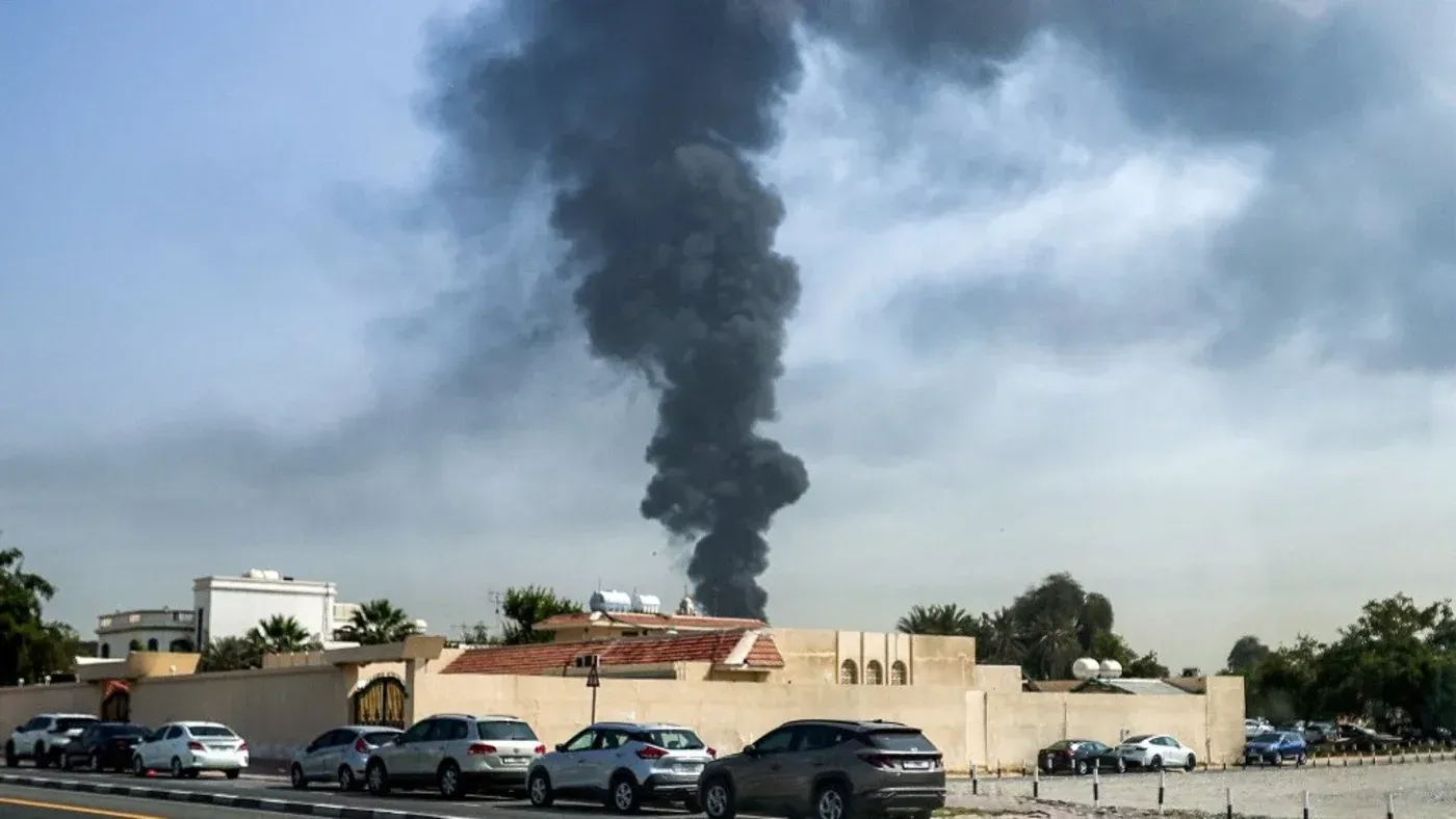 تصاعد دخان كثيف من موقع حريق في دبي، مع وجود سيارات متوقفة على جانب الطريق، مما يعكس تأثير الحرب على المدينة.