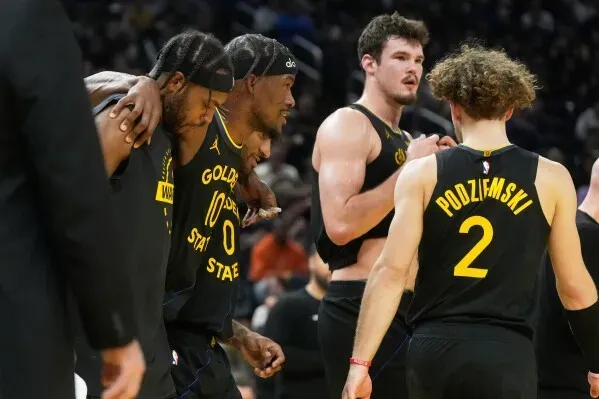 جيمي باتلر يخرج من الملعب بمساعدة زملائه بعد إصابته في الركبة خلال مباراة ضد ميامي، حيث يظهر التعبير القلق على وجهه.