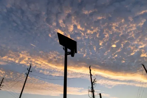 كاميرا قارئ لوحات السيارات الآلي مثبتة على عمود تحت سماء ملبدة بالغيوم، مع تداخل خطوط الكهرباء في الخلفية.