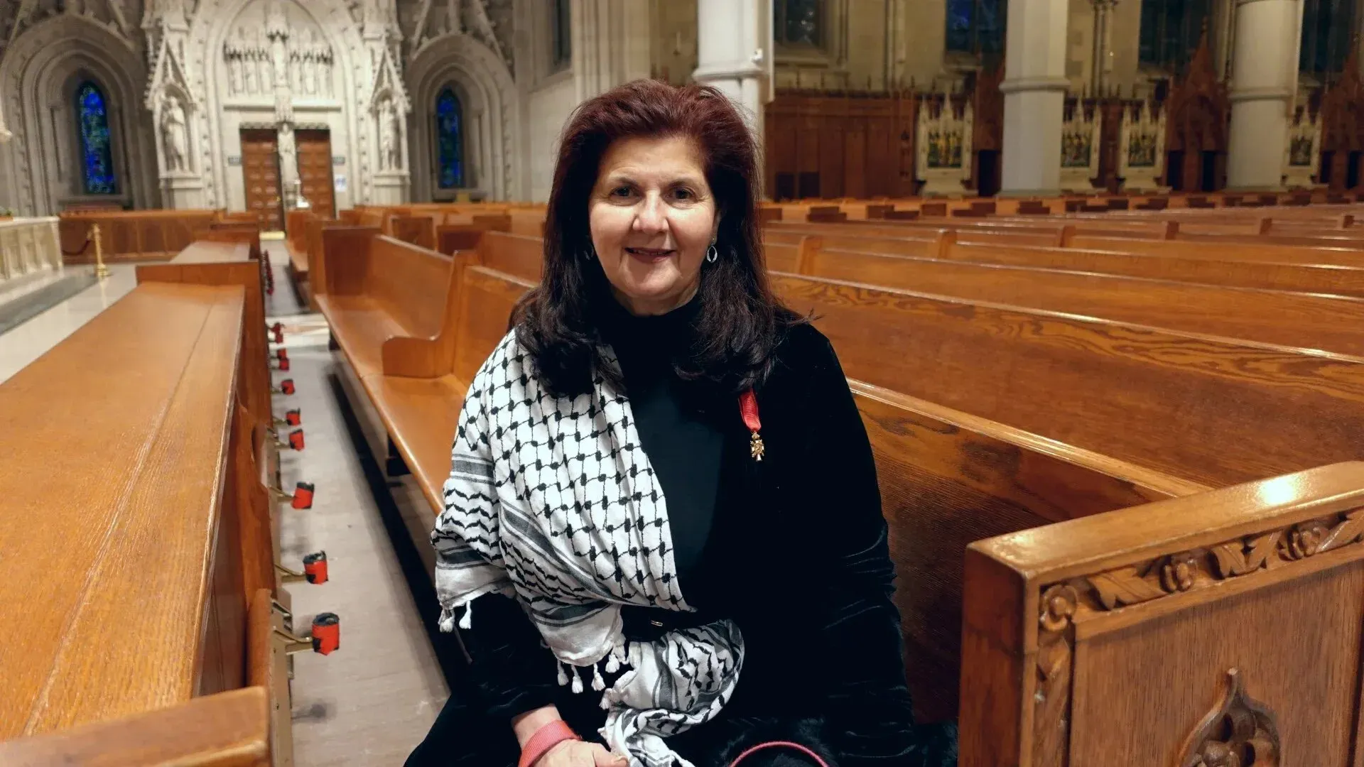 امرأة تجلس في كاتدرائية القلب الأقدس، ترتدي وشاحًا يحمل الألوان الفلسطينية، تعبر عن حزنها بعد وفاة البابا فرنسيس.