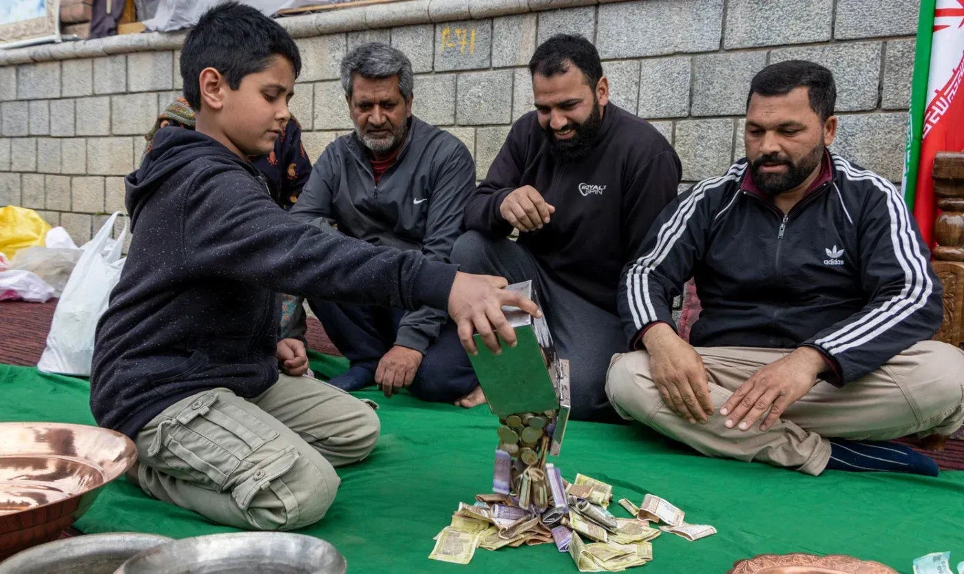 طفل يجمع التبرعات النقدية في كشمير، محاط بالمتطوعين، في حملة دعم إنسانية لصالح إيران خلال عيد الفطر.