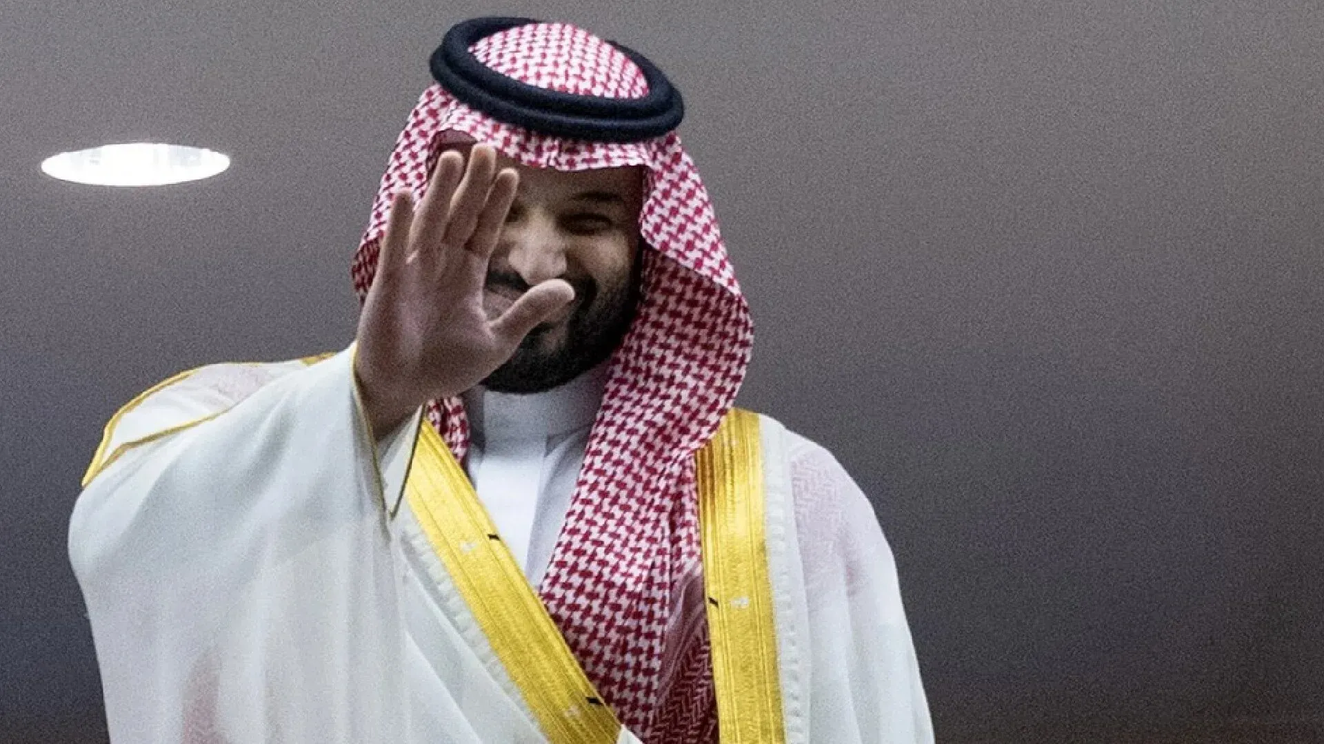 صورة لمجموعة من الرجال يرتدون ملابس تقليدية، يلوح أحدهم بيده في إشارة وداع، مع خلفية تشير إلى حدث رسمي في السعودية.