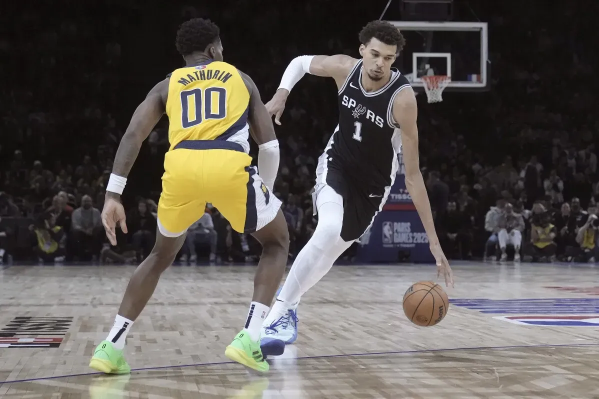 فيكتور ويمبانياما يت dribble الكرة خلال مباراة في دوري NBA، بينما يلعب ضد بينيديكت ماثورين في ملعب باريس، وسط حماس الجماهير.