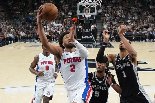 لاعب من فريق ديترويت بيستونز يسجل نقطة بينما يحاول لاعبان من سان أنطونيو سبيرز صد الكرة، في مباراة مثيرة بالدوري الأمريكي للمحترفين.