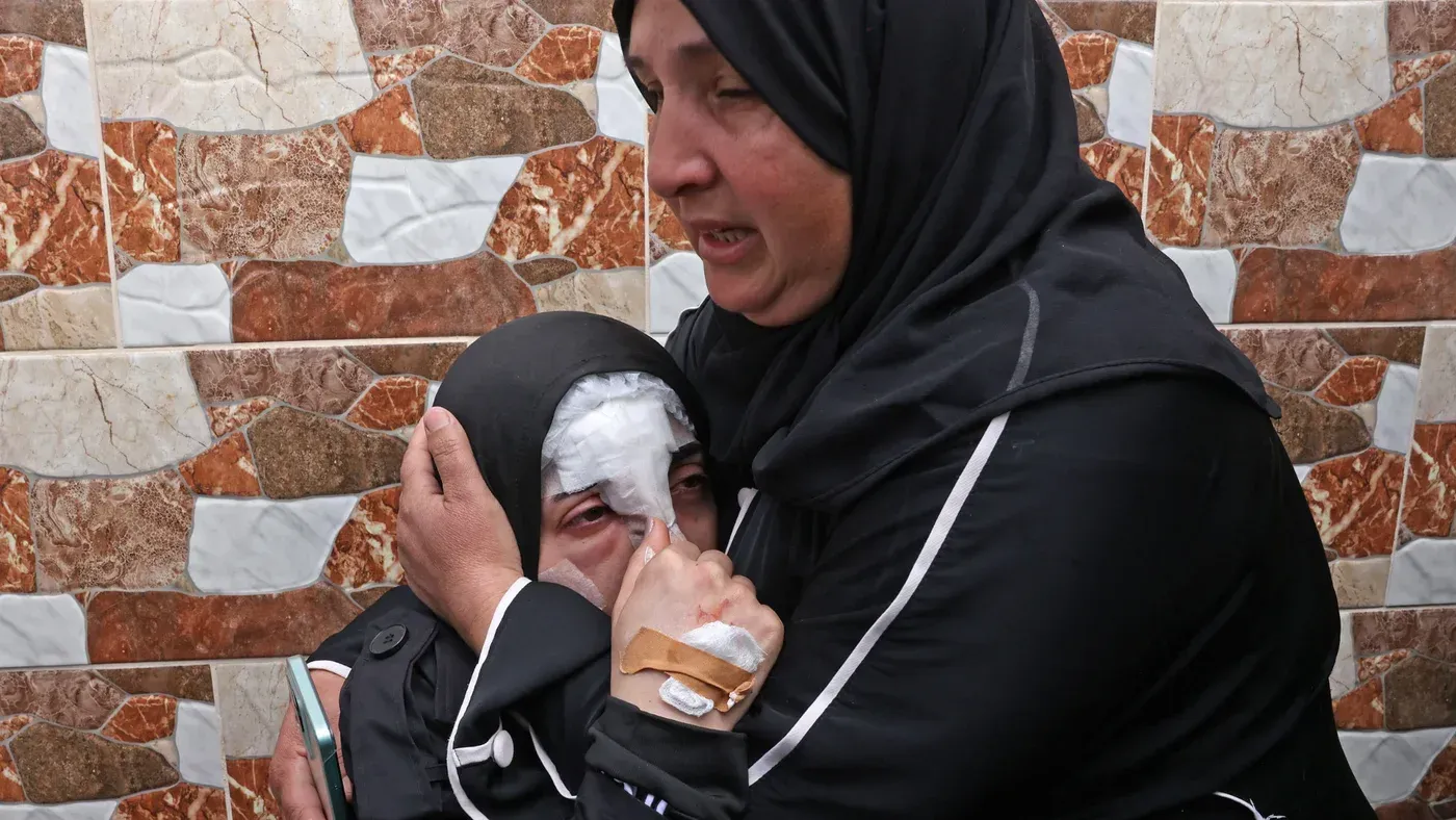 هديل المسالمة، فتاة فلسطينية تعاني من آثار غارة، تحتضنها والدتها في لحظة حزن، مع خلفية جدارية ملونة.