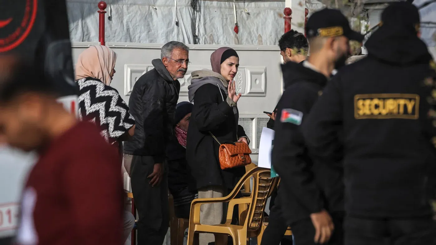 مجموعة فلسطينية تنتظر أمام مبنى في غزة وسط تواجد أفراد أمن، تعكس الأوضاع اليومية والتحديات الحياتية في ظل الاحتلال.