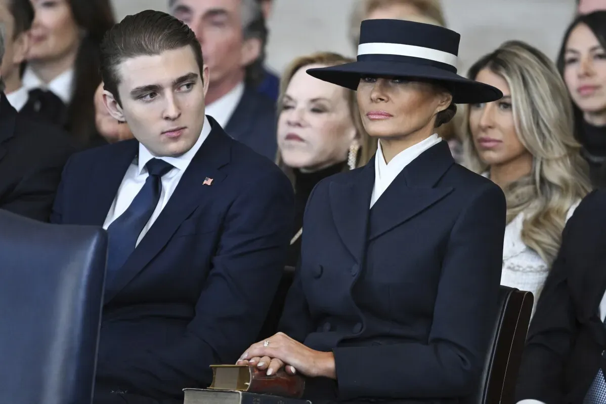 ميلانيا ترامب seated wearing a wide-brimmed navy hat and a coordinated outfit, attending her husband's inauguration ceremony, embodying elegance and tradition.