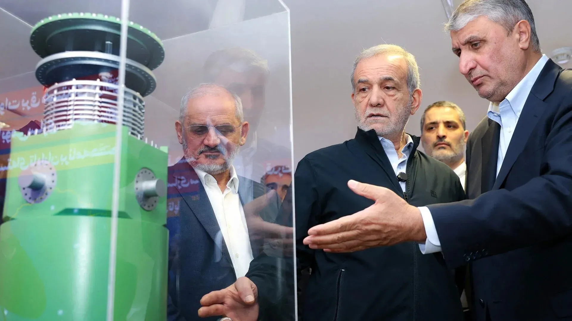 رجلان يتحدثان أمام نموذج لجهاز نووي في معرض إيراني، مما يعكس تطورات البرنامج النووي الإيراني وتأثيره على المحادثات الدبلوماسية.