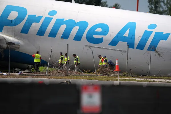 طائرة شحن تابعة لـ Amazon Prime Air تجاوزت مدرج مطار Miami، وفريق تحقيق يرتدي سترات أمان يفحص موقع الحادث.