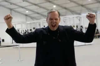 شخص يحتفل بحماس في موقع حفل افتتاح أولمبياد كورتينا في ميلانو، مع توقعات لعرض مميز ومشاركة فنانين عالميين.