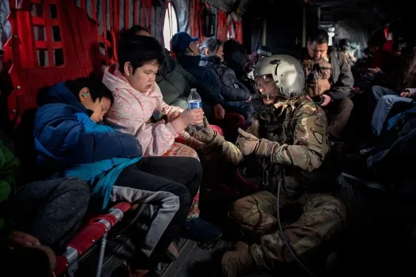 جنود يساعدون أطفالًا نازحين في طائرة عسكرية، حيث يتم تقديم المياه والدعم أثناء عملية الإجلاء من القرى المتضررة في ألاسكا.