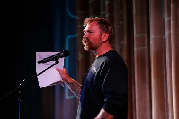 غراهام بلاتنر، مرشح لمجلس الشيوخ من ولاية ماين، يتحدث في حدث عام، ممسكًا بأوراق، مع التركيز على قضايا الحملة والجدل حول ماضيه.