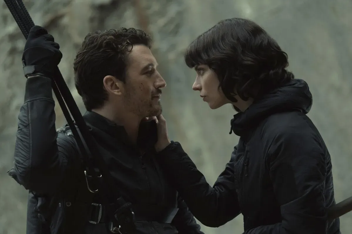 مشهد من فيلم "The Gorge" يظهر شخصين في موقف حميم، يرتديان ملابس داكنة، بينما يتبادلان النظرات في بيئة جبلية.