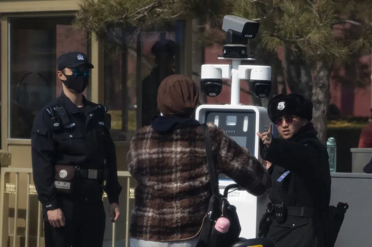 ضباط شرطة يرتدون زيًا رسميًا يتحدثون مع امرأة في موقع المؤتمر الوطني لنواب الشعب الصيني، مع وجود كاميرات مراقبة خلفهم.