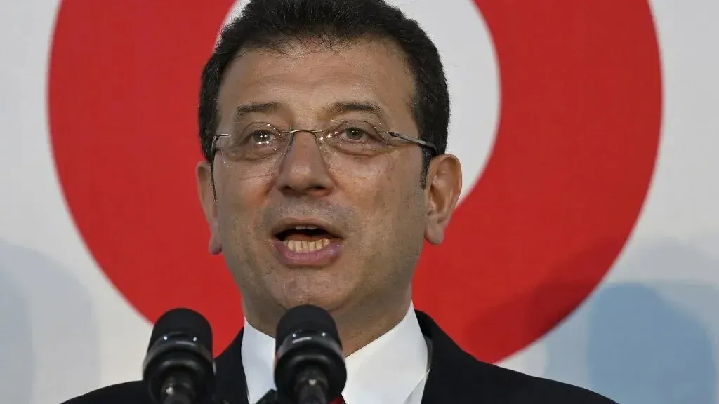 أكرم إمام أوغلو، رئيس بلدية إسطنبول، يتحدث أمام ميكروفونات، مع خلفية تحمل شعار تركيا، في سياق اعتقاله بتهم الفساد.