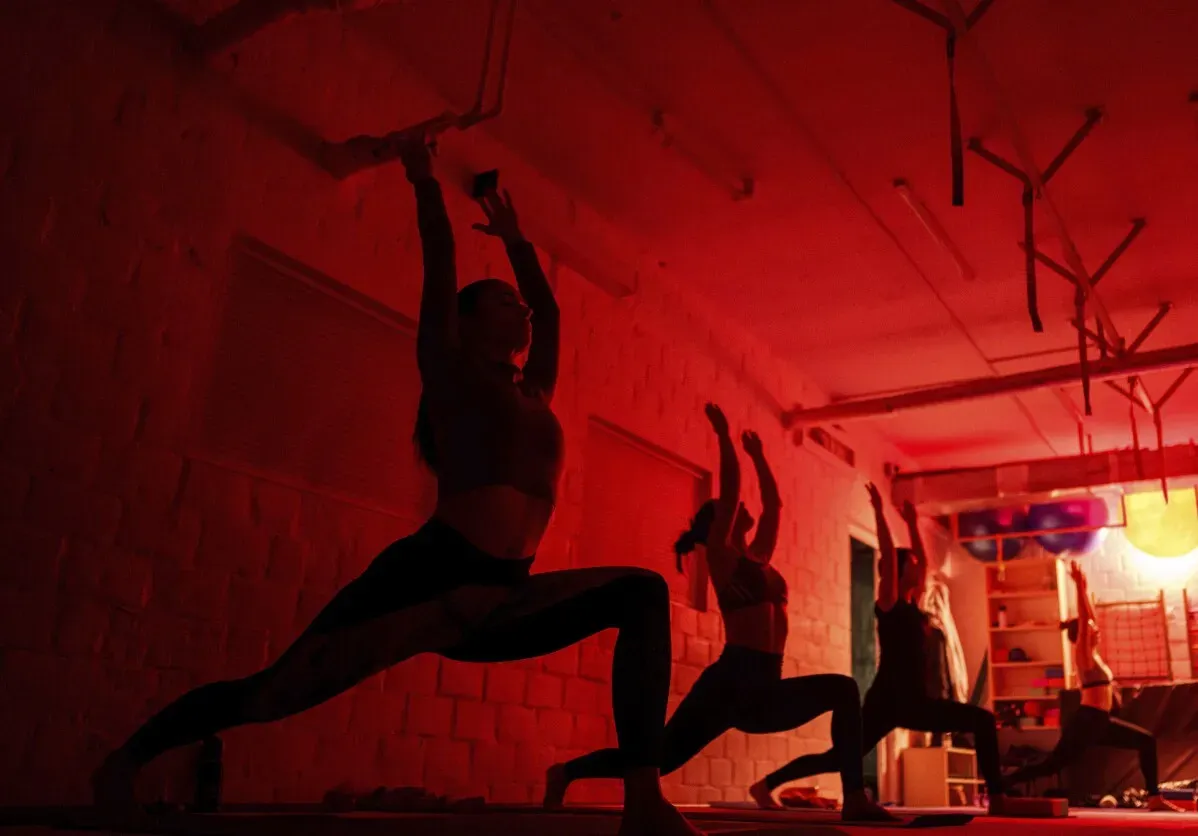 مجموعة من ممارسي اليوغا في حصّة تتدرب تحت إضاءة حمراء، يقومون بأوضاع ديناميكية تعكس توازن الجسد والعقل.