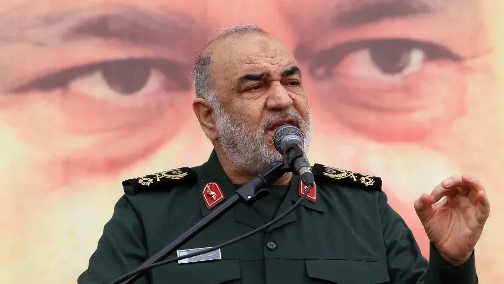 اللواء حسين سلامي، قائد الحرس الثوري الإيراني، يتحدث في مؤتمر، مع صورة خلفية تعكس التوترات العسكرية في المنطقة.