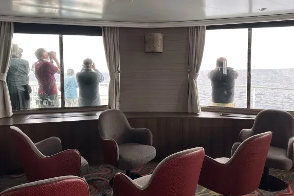 ركاب السفينة MV Hondius يراقبون البحر من داخل صالة، مع وجود كراسي مريحة حولهم، وسط أجواء من القلق بشأن فيروس الهانتا.