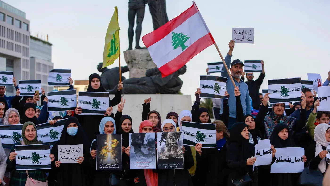 مظاهرة في لبنان تضم مجموعة من النساء والرجال يحملون لافتات تدعو إلى المقاومة، مع العلم اللبناني في المقدمة، خلفهم تمثال.