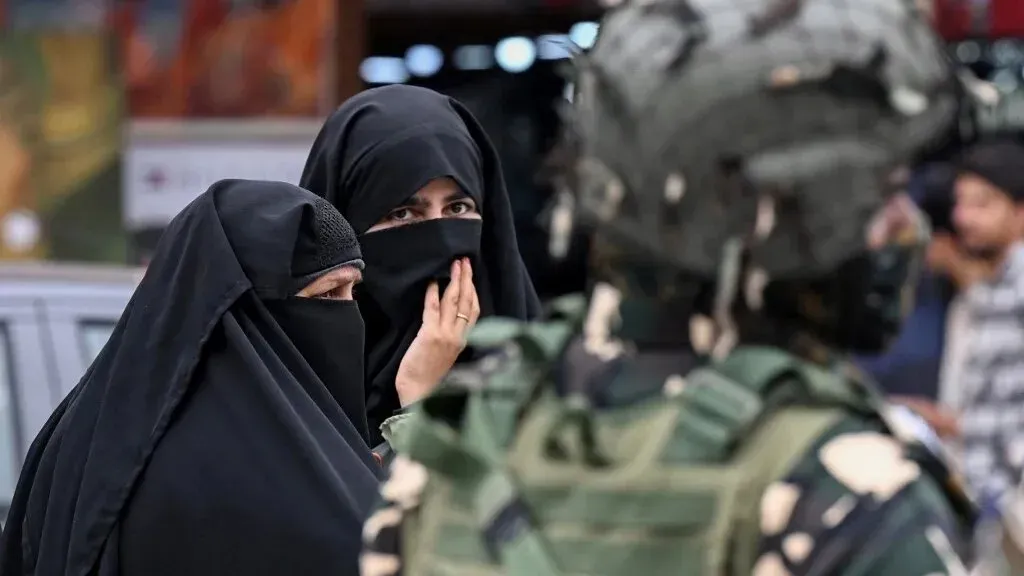 امرأتان ترتديان الحجاب يتحدثان مع جندي مسلح في منطقة تشهد توترًا سياسيًا، مما يعكس الصعوبات التي تواجه المسلمين في الهند.