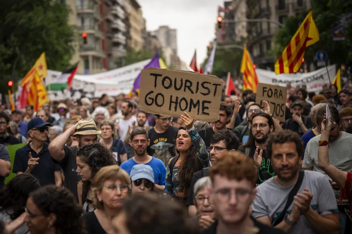 محتجون في برشلونة يحملون لافتات تعبر عن استيائهم من السياحة الجماعية، مع شعارات مثل \"السياح اذهبوا إلى منازلكم\".