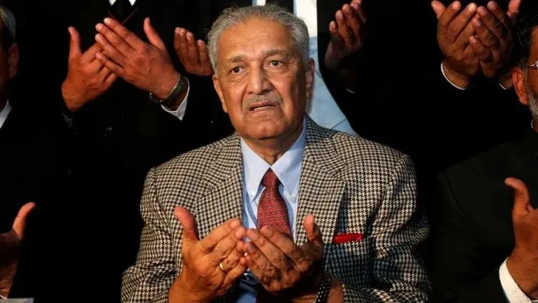 عبد القدير خان، أبو البرنامج النووي الباكستاني، يظهر أثناء الدعاء، محاطًا بأشخاص آخرين، معبرًا عن مكانته كرمز وطني.