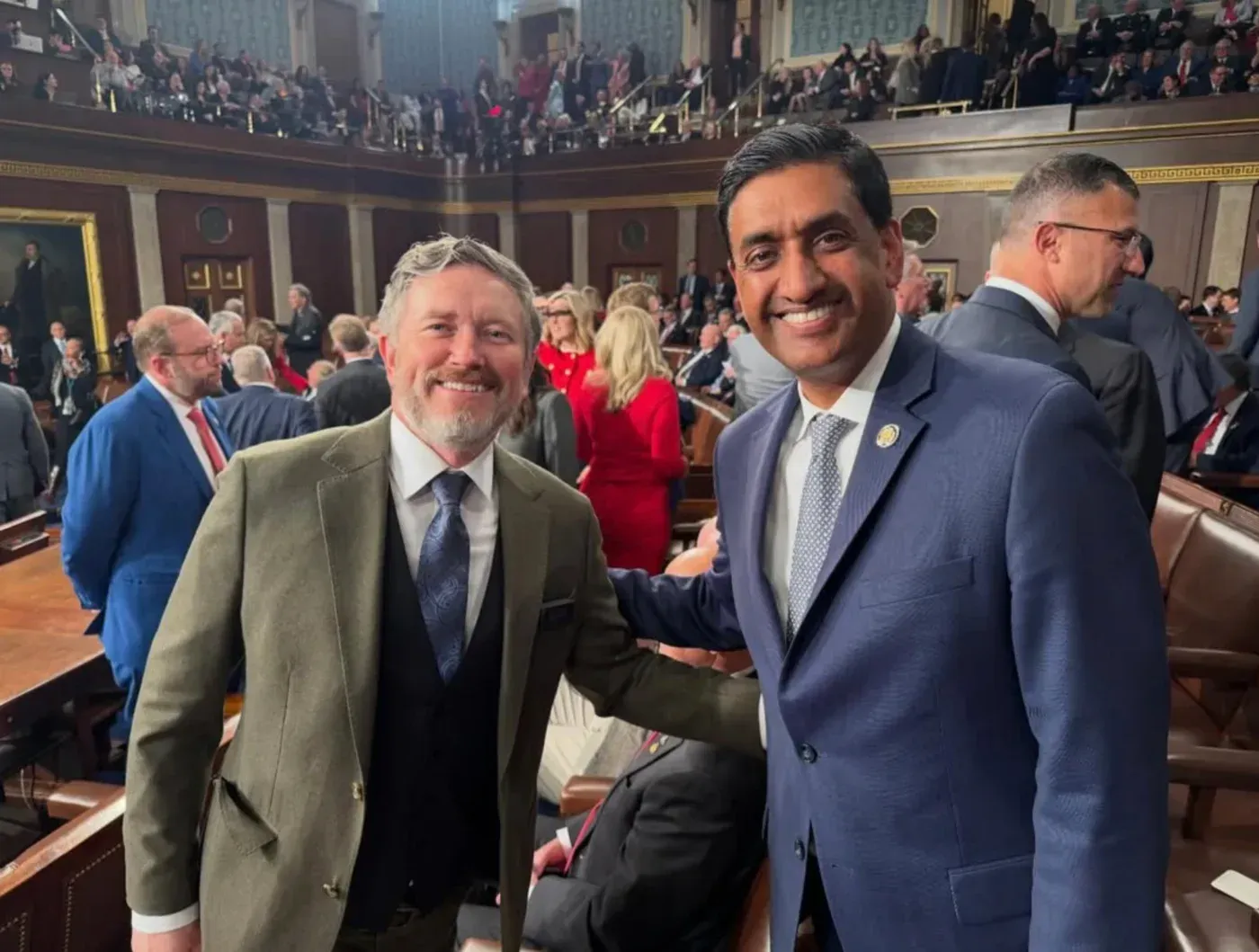 عضو الكونغرس رو خانا وعضو الكونغرس توماس ماسي يتصافحان في قاعة مجلس النواب خلال خطاب حالة الاتحاد، مع خلفية من الحضور.