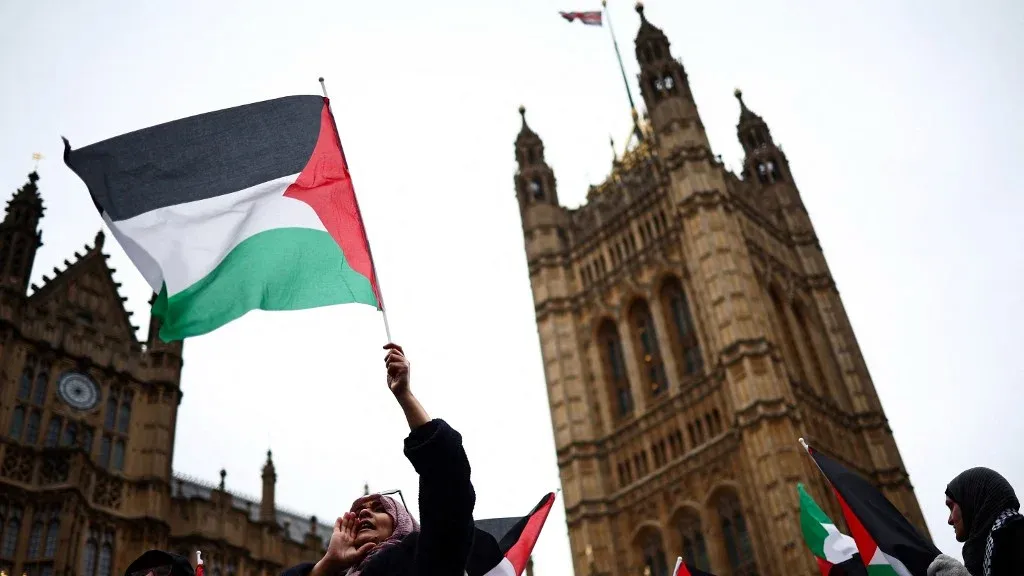امرأة تحمل العلم الفلسطيني أمام مبنى البرلمان البريطاني، تعبيرًا عن الاحتجاج ضد بيع الأراضي الفلسطينية.