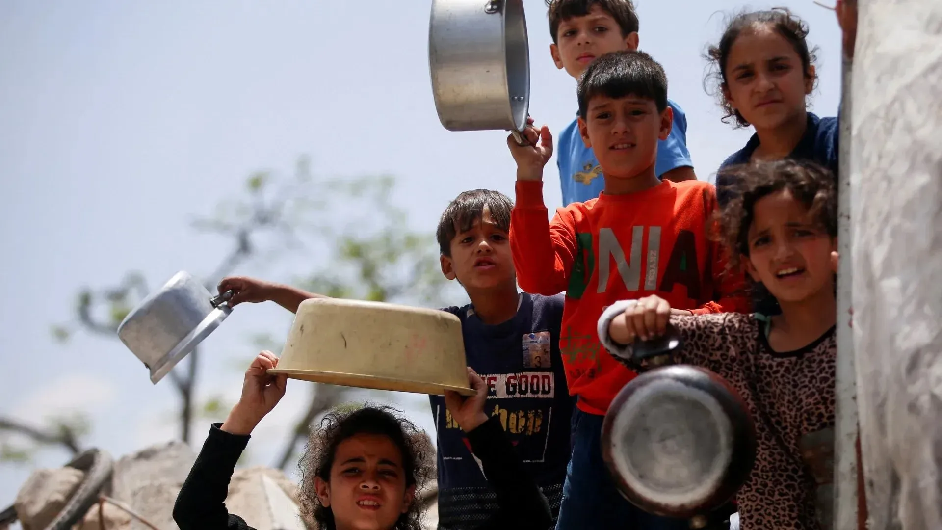 أطفال فلسطينيون في غزة يحملون أواني معدنية، معبرين عن معاناتهم في ظل الظروف الصعبة التي يعيشونها.