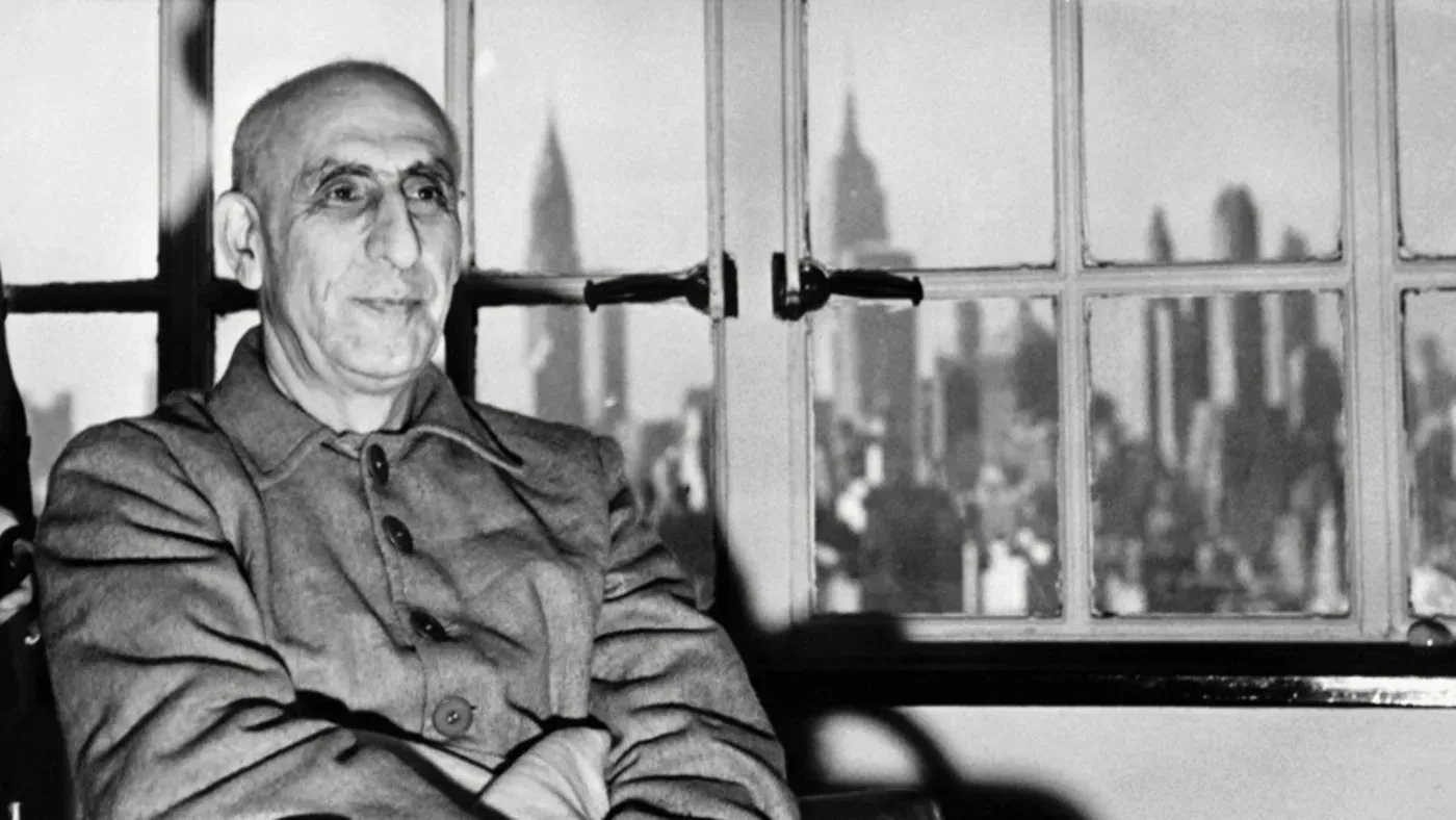 محمد مصدق، رئيس الوزراء الإيراني السابق، يجلس أمام نافذة تطل على مدينة نيويورك، مع خلفية معالم المدينة.