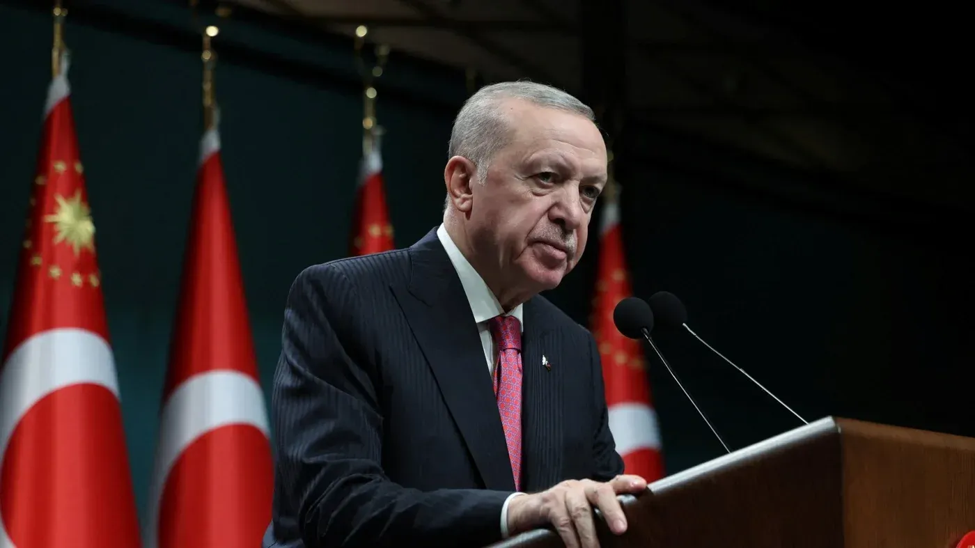 إردوغان يتحدث في مؤتمر صحفي، مع وجود الأعلام التركية خلفه، مما يعكس دور تركيا المركزي في السياسة الإقليمية.