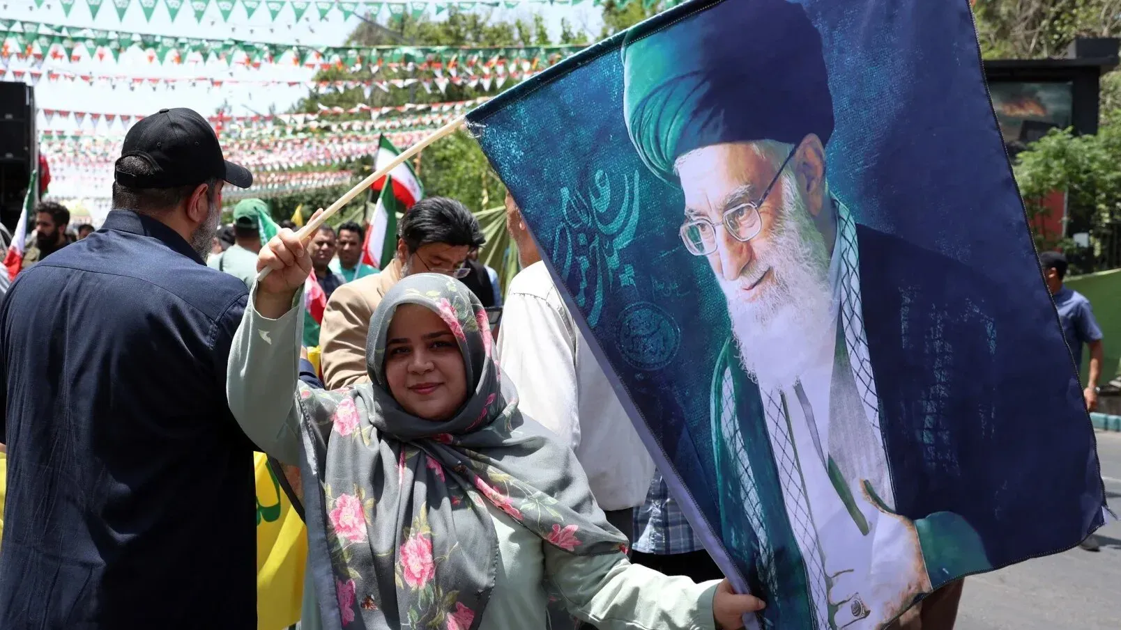 امرأة تحمل علمًا يحمل صورة المرشد الأعلى الإيراني آية الله علي خامنئي، وسط تجمع حاشد في إيران.