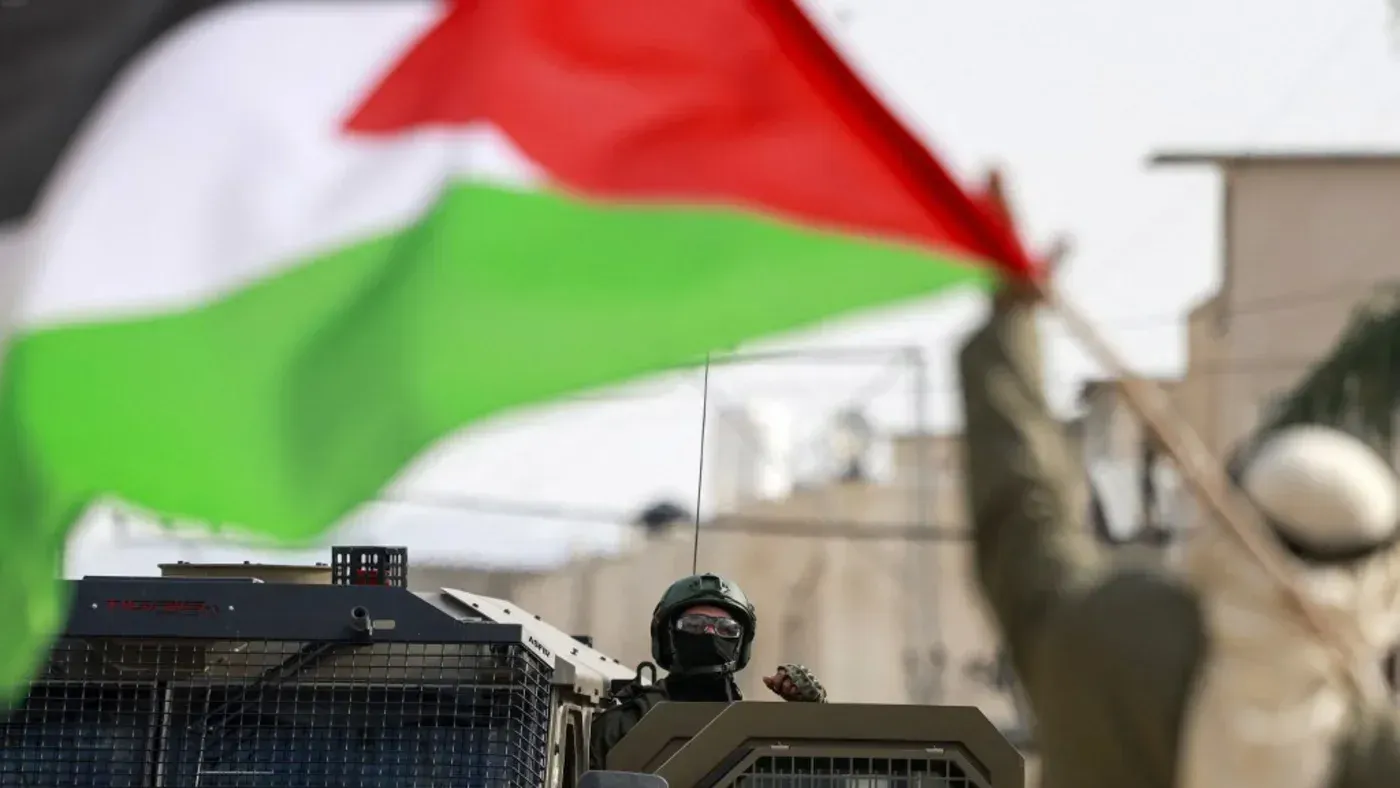 محتج يحمل علم فلسطين أمام مركبة عسكرية، مع تواجد عناصر أمنية، في سياق التوترات المستمرة في الأراضي المحتلة.