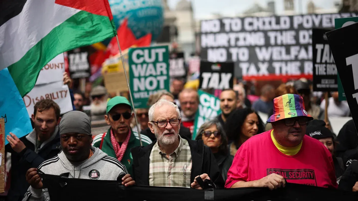محتجون في مسيرة لدعم حقوق الفلسطينيين، يحملون لافتات ضد الفقر والحرب، مع ظهور شخصية بارزة في المقدمة.