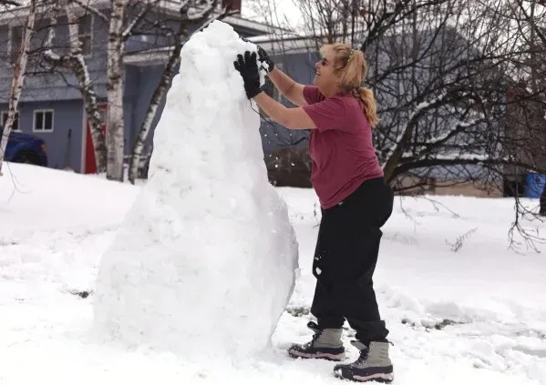 امرأة تعمل على تشكيل كومة من الثلج في حديقة منزلها خلال طقس شتوي قاسٍ في نيو إنجلاند، حيث تتساقط الثلوج والأمطار المتجمدة.