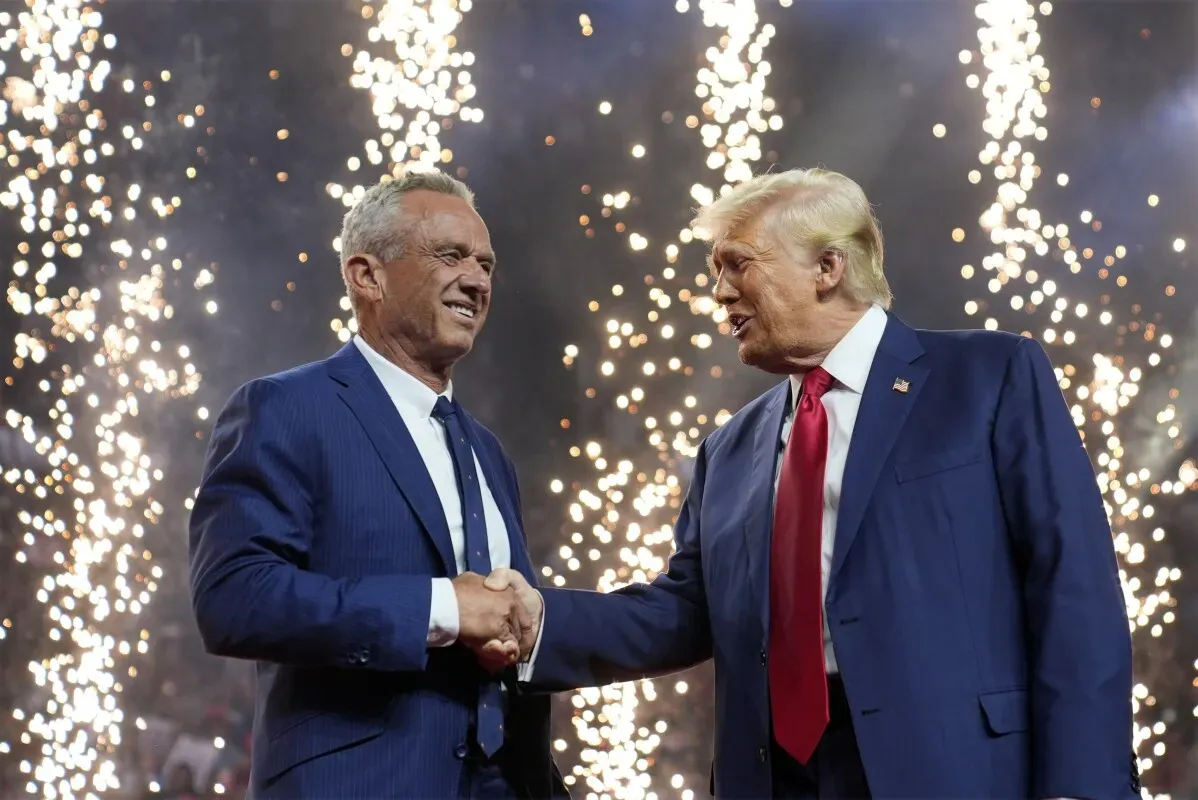 مصافحة بين روبرت كينيدي الابن ودونالد ترامب، مع خلفية من الألعاب النارية، تعكس التحالفات السياسية في الانتخابات.