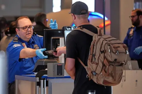 موظف أمن في مطار يتفاعل مع مسافر يحمل حقيبة ظهر، وسط أجواء مزدحمة تعكس تحديات السفر الجوي في الوقت الراهن.