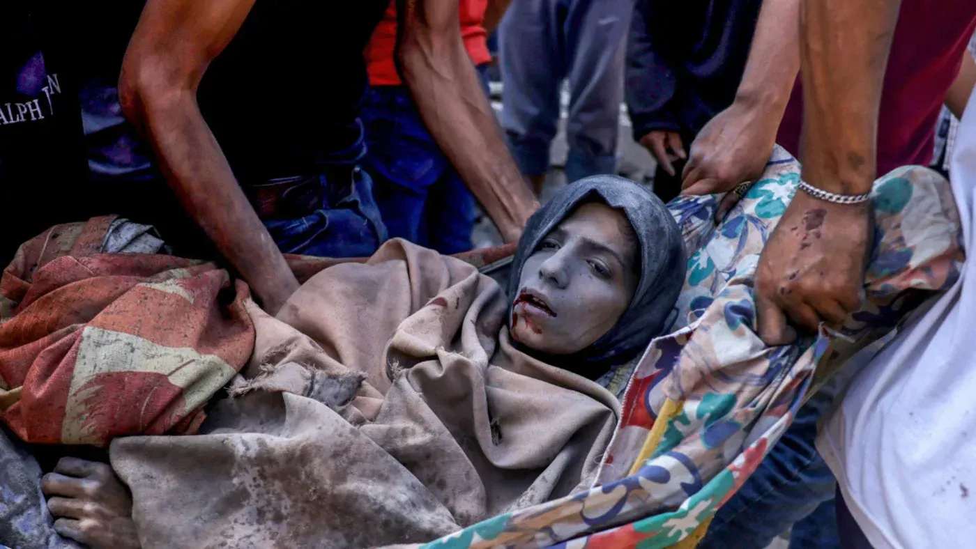 شخصان يحملان جثة امرأة مصابة بجروح خطيرة في غزة، تعكس المعاناة الإنسانية المتزايدة نتيجة النزاع والمجاعة.
